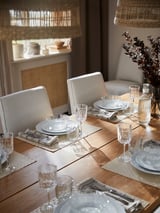 Moderne eettafel met witte stoelen, helder glaswerk en borden. Neutrale tinten, natuurlijk hout en elegant design.