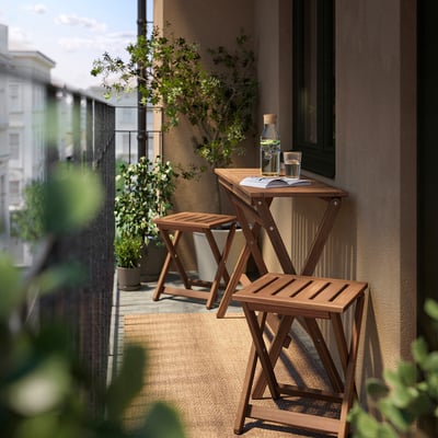 Klein balkon met NÄMMARÖ bruine houten tafel en krukken, glazen karaf en planten.