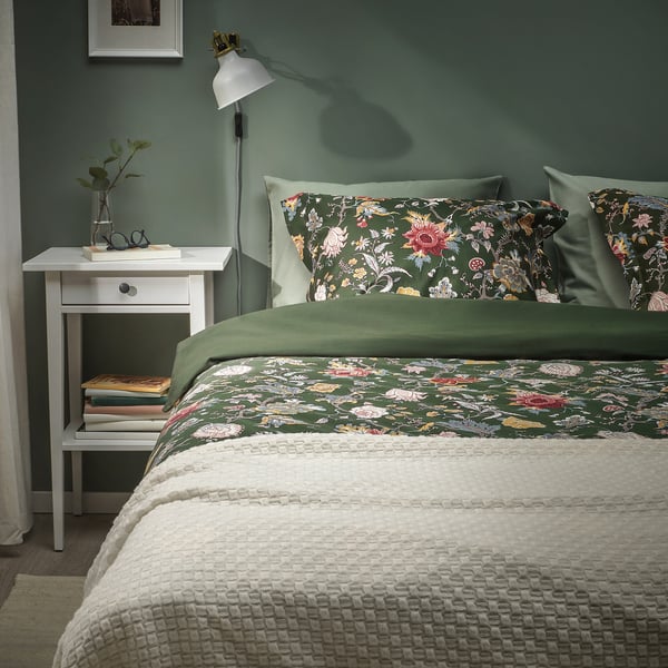 Gezellige slaapkamer met donkergroen gebloemd dekbed, wit nachtkastje en groen.