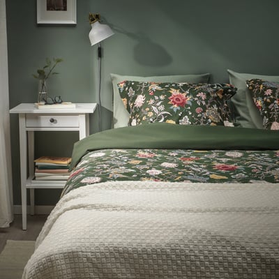 Slaapkamer met groene muren, wit nachtkastje met boeken en vaas. Twin bed met donkergroen bloemen NÄSSELKLOCKA dekbed & kussenslopen, wit dekbed.