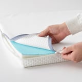 Een persoon ritst een matrasbeschermer met koele en warme zijkanten voor comfort en laat de afneembare hoes zien.