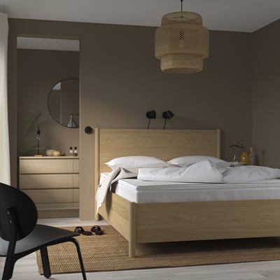 Minimalistische slaapkamer met houten bed, nachtkastjes, zwarte stoel en hanglamp.