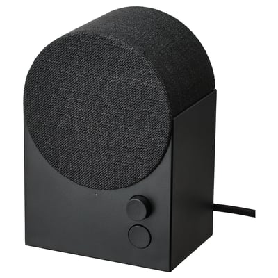 Zwarte, met stof beklede luidspreker met een afgeronde bovenkant, minimalistisch ontwerp, kleine draaiknop en knop aan de voorkant, bedraad aan de achterkant. NATTBAD bluetooth luidspreker.