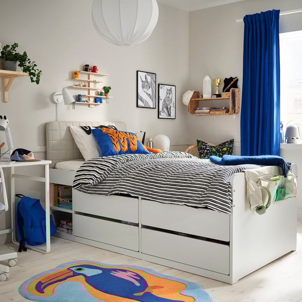 Bed met zebraprint, boeken, speelgoed, blauw vloerkleed, bureau, stoel, blauwe gordijnen.
