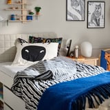 Bed met dekbed met zebraprint, kleurrijke kussens, kunst aan de muur van een eekhoorn en vos, en blauwe deken.