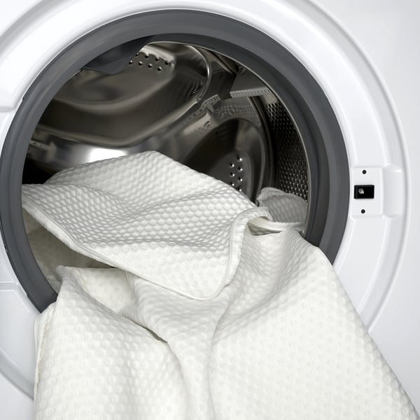 Wit traagschuim matrasbeschermer in wasmachine voor eenvoudige reiniging.