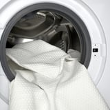 Wit traagschuim matrasbeschermer in wasmachine voor eenvoudige reiniging.