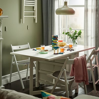 Moderne eethoek met NORDEN-tafel, opklapbare stoelen en gestapeld blokspel bij een raam met een hanglamp.