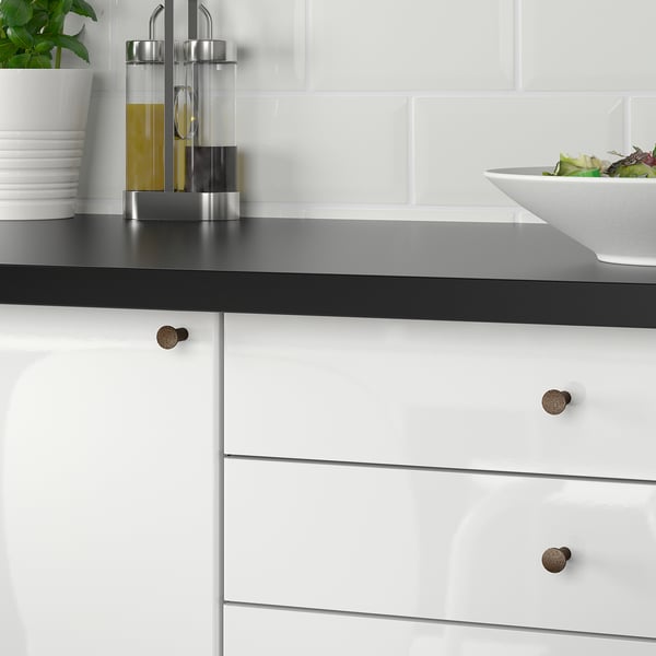 Moderne keukenkasten, zwart aanrechtblad, witte lades met bronzen handgrepen, slakom.