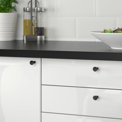 Een moderne keuken met witte kasten en zwarte werkbladen met zwarte NYDALA-knoppen, die de kaststijl verbeteren. Op het strakke aanrecht staat een slakom.