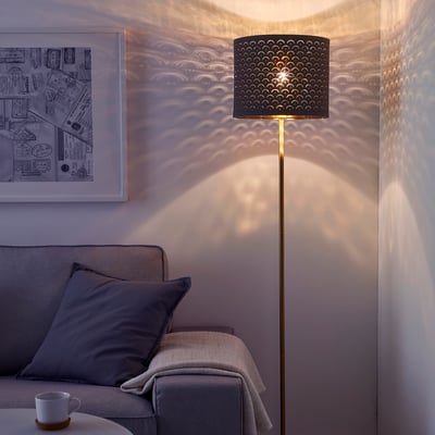 Stijlvolle vloerlamp met geperforeerde kap werpt lichtpatronen en voegt warmte toe in de buurt van de bank.