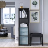 Moderne woonkamer met een zwarte PANSARTAX boekenkist, blauwe meubels en grote ramen.
