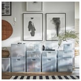 Doorzichtige kunststof opbergcontainers met deksel, netjes gestapeld. Abstracte kunst aan de muur, zwart-wit gestreept tapijt, gevlochten manden en hanglamp.