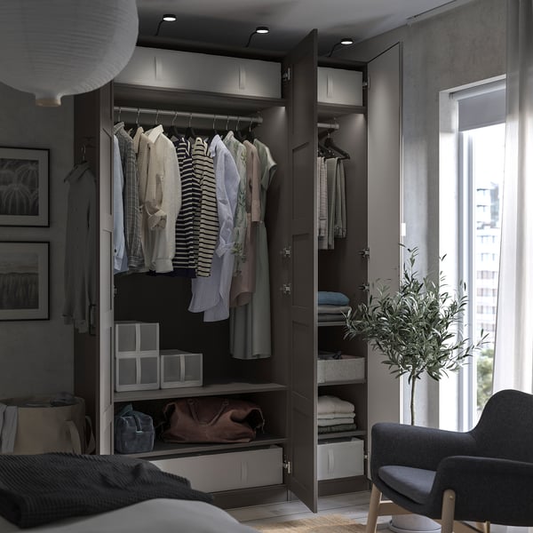 Moderne slaapkamer met open kledingkast, georganiseerde kleding, grijze stoel en plant.