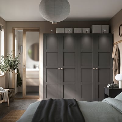 Moderne slaapkamer met zwarte PAX kledingkast, grijze handgrepen en opbergruimte op het blad. Gezellig bed met blauwe deken, lantaarnlicht en groene plant.