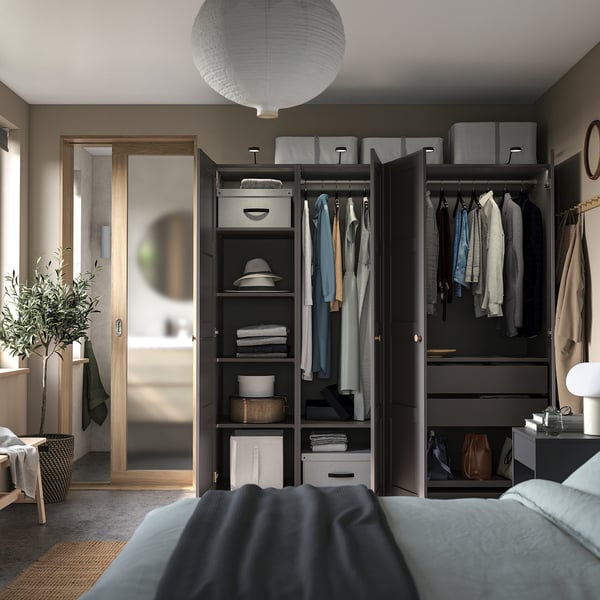 Moderne slaapkamer met zwarte PAX kledingkast, hangende kleding, planken en een grote spiegel. Grijs bed en lichtpunt.