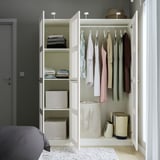 Open witte kledingkast met planken, kleding en opbergbakken.