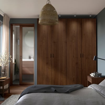 Moderne slaapkamer met grote houten PAX kledingkast met donker walnootfineer, grijs beddengoed en geweven hanglamp.