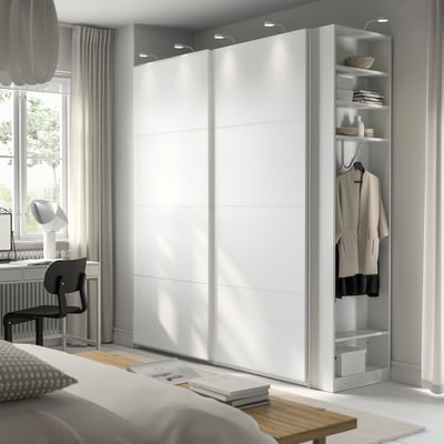 Minimalistische slaapkamer met witte PAX kledingkast, schuifdeuren, ingebouwde verlichting, gezellig bed en eenvoudige inrichting.