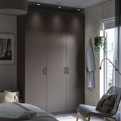 Moderne slaapkamer een grijze PAX kledingkast met strakke handgrepen, wit bed en een stoel bij het raam met uitzicht op de stad.