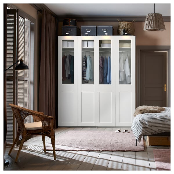 Moderne slaapkamer met PAX kledingkast met glazen front, stoel, vloerkleed en gestreept bed. Houten vloer, beige muren, groot raam.