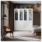 Moderne slaapkamer met PAX kledingkast met glazen front, stoel, vloerkleed en gestreept bed. Houten vloer, beige muren, groot raam.