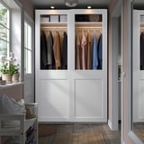 Open witte kledingkast, PAX, met kleding, staat hoog naast het raam en de bank. Modern en ruim.