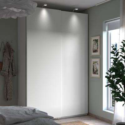 Minimalistische slaapkamer met witte PAX-kledingkast, grijze muren, natuurlijk licht uit het raam, ingelijste kunst en kamerplant.