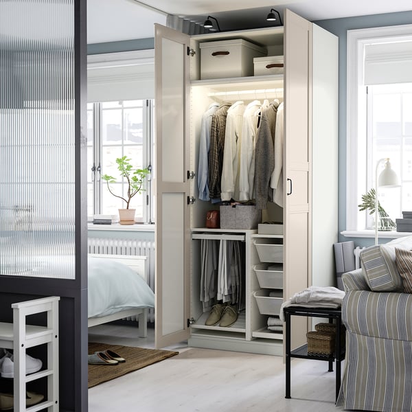 Open kledingkast met kleding, planken en opbergdozen, met spiegeldeur die bed en raam weerspiegelt.