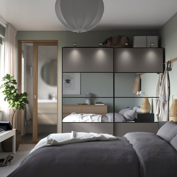 Moderne slaapkamer met grijze PAX kledingkast, spiegeldeuren, wit beddengoed en een hangplant.