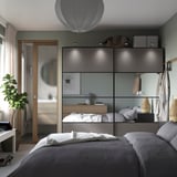 Moderne slaapkamer met grijze PAX kledingkast, spiegeldeuren, wit beddengoed en een hangplant.