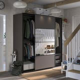 Moderne kast met schuifdeuren en hangende kleding. Goed verlicht, georganiseerd met planken en opbergbakken. Rechts is een trap zichtbaar.
