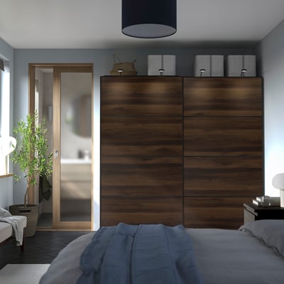 Moderne slaapkamer met PAX kledingkast, schuifdeuren en opbergruimte aan de bovenkant. Bed met blauwe deken op de voorgrond.