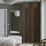 Moderne slaapkamer met hoge donkere PAX kledingkast, spiegel, bank en gedeeltelijk zichtbaar bed.