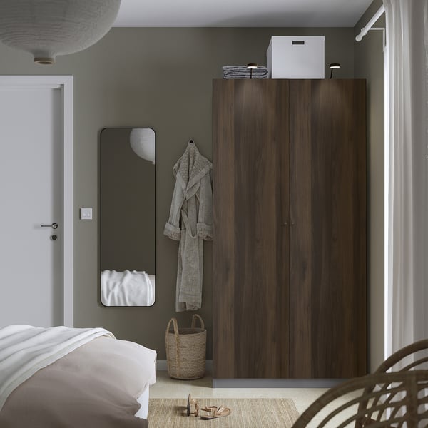 Minimalistische slaapkamer met grote donkerhouten PAX-kast naast een wit bed, grijze muren en een hangende badjas.
