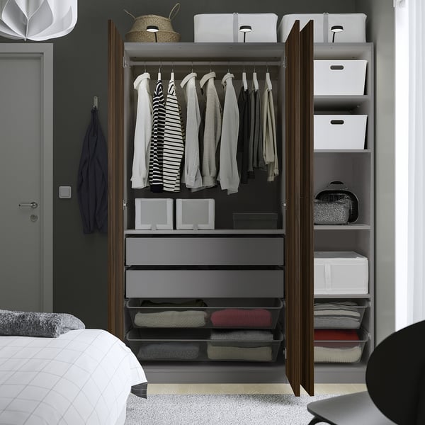 Open kledingkast met hangende overhemden, opgevouwen kleding in lades en opbergdozen op planken.