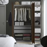 Open kledingkast met hangende overhemden, opgevouwen kleding in lades en opbergdozen op planken.