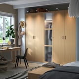 Moderne slaapkamer met grote lichthouten PAX kast, zwarte bureaustoel, gestreept vloerkleed en zwart bedframe.