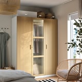 PAX kledingkast in slaapkamer met glazen deur, manden, rieten stoel, natuurlijk licht.