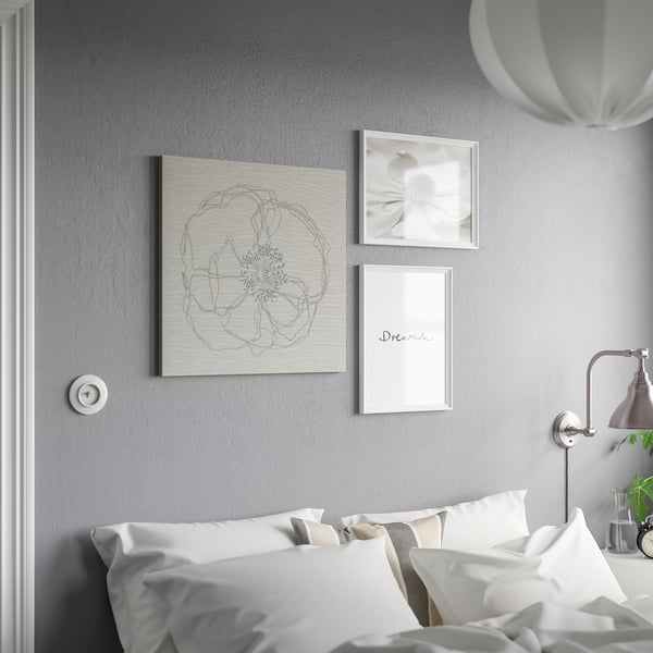 Wit bed met kussens tegen grijze muur, drie ingelijste kunstwerken, witte lamp.