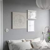 Wit bed met kussens tegen grijze muur, drie ingelijste kunstwerken, witte lamp.