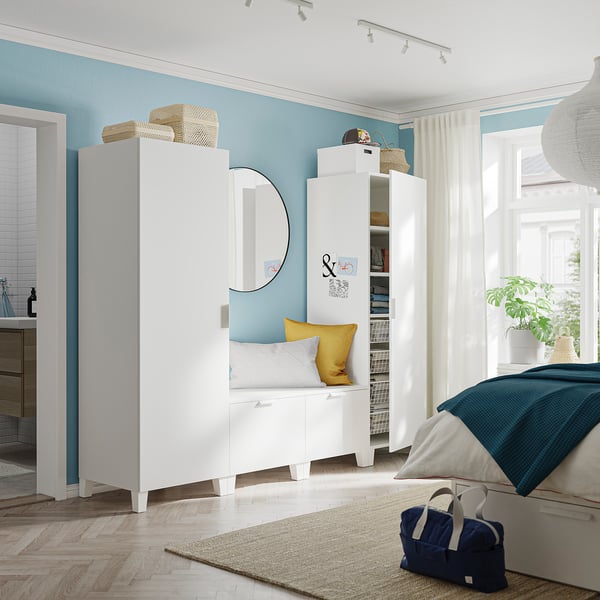 Lichte, moderne slaapkamer met witte PLATSA opbergmeubels, blauwe muren en een bed met marineblauwe en gele accenten.