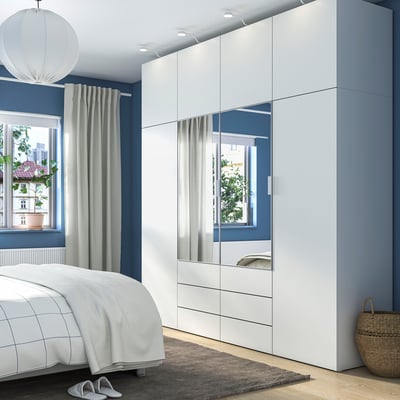 Moderne slaapkamer met witte PLATSA opbergkast, spiegeldeuren, geruit bed, grijze gordijnen, rieten mand.