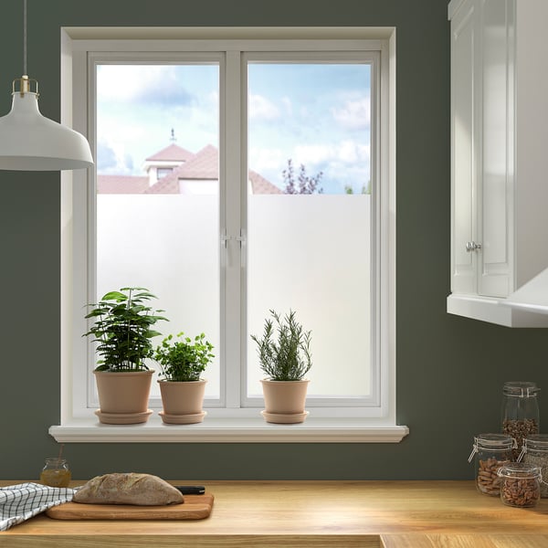 Keukenraam met kruiden, moderne huizen, blauwe hemel. Donkere muren, witte kasten, houten aanrechtblad met brood.