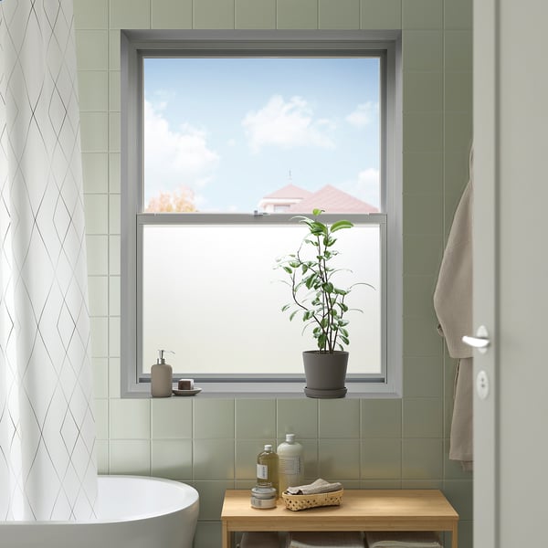 Moderne badkamer met groot raam met neutraal getinte PUCKELFLY raamfolie, plant en handdoek.