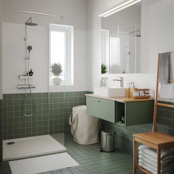 Moderne badkamer met groene tegels, wit bad, glazen douche en bamboe plank met stoel en handdoekenrek.