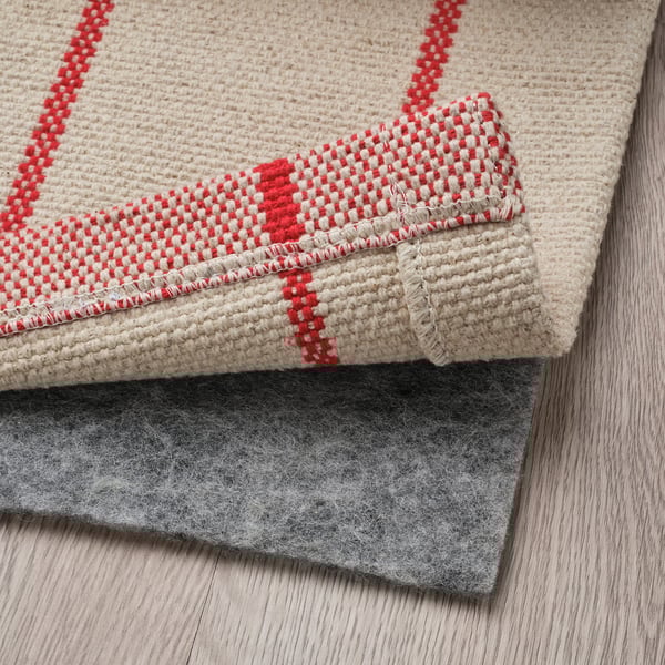 Rood en beige gestreept vloerkleed gevouwen, onderlaag zichtbaar, wat het gebruik en het ontwerp laat zien.