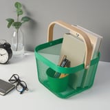Groene gaasopbergmand met houten handvat, met mappen en pennen, naast een klok en vaas.