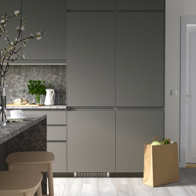 Moderne keuken met grijze kasten, aanrechtinrichting en een grote papieren zak naast een houten stoel.
