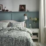Gezellige slaapkamer met groenblauwe muren, paisley bed, verse bloemen, zacht licht.